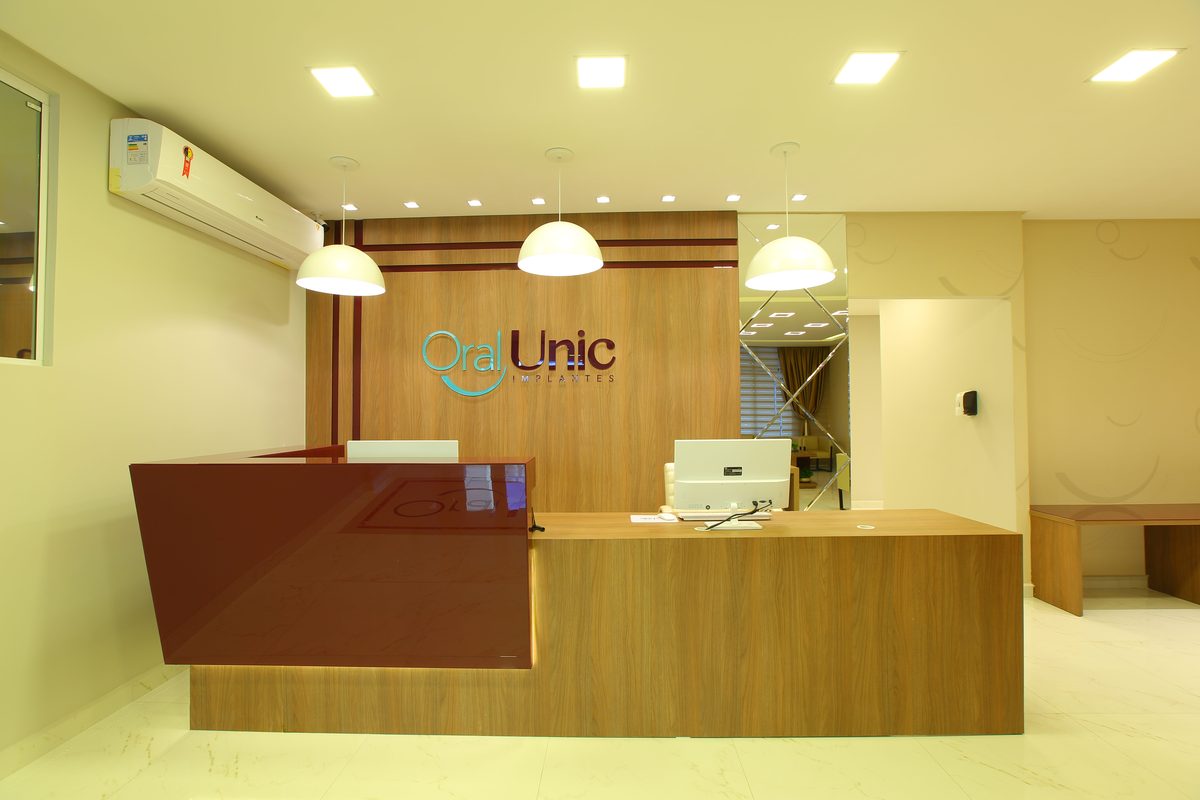 Recepção da Oral Unic Lajeado, com o logo da rede no painel de madeira